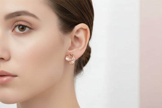 A pair of gold-toned bow-shaped stud earrings with small clear rhinestone accents, displayed on a white XUPING card over a white beaded tray and pink satin fabric.