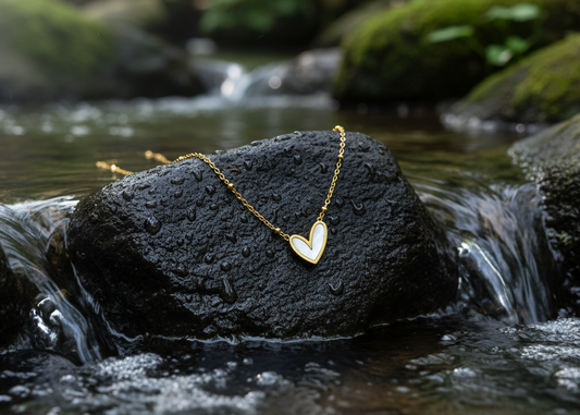 A gold heart pendant necklace with a white inlay, resting on a draped pink satin fabric background.
