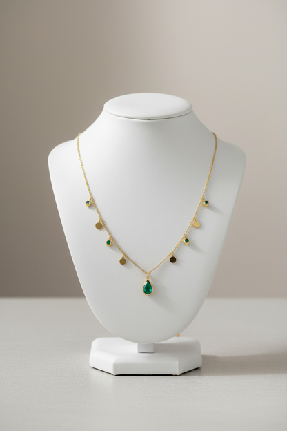 A delicate gold chain necklace featuring a teardrop-shaped green gemstone pendant at the center, with small gold disc charms and a few tiny green stone accents along the chain, displayed on a clean white background.