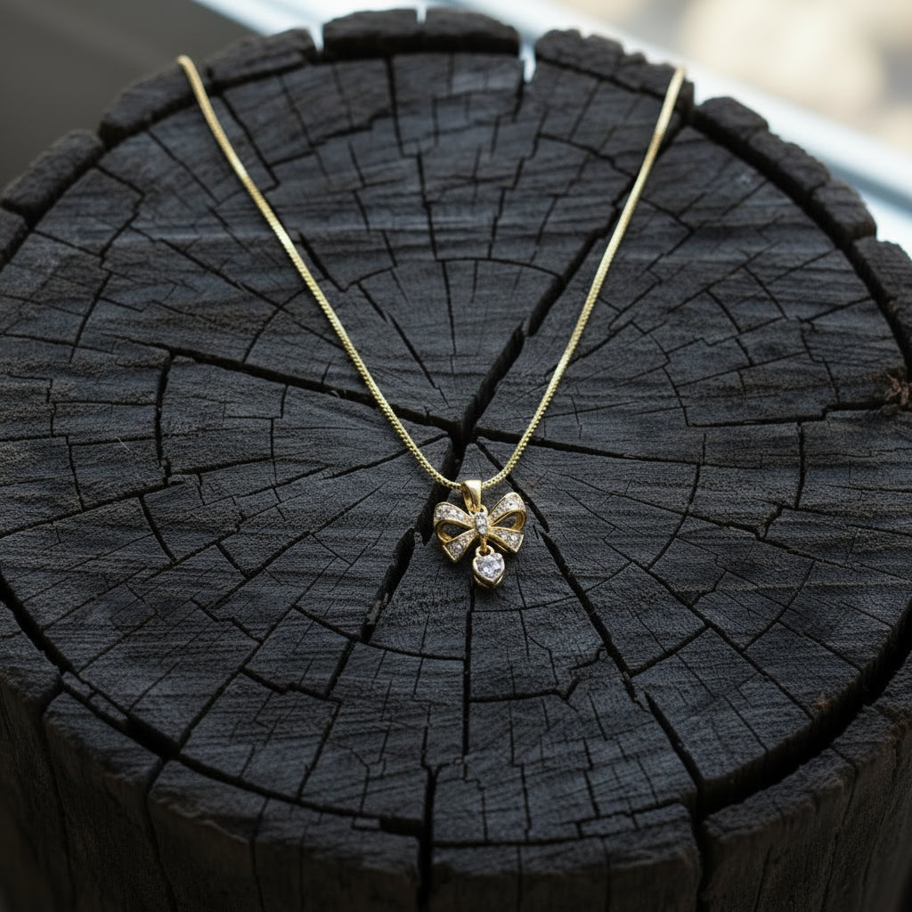 A gold necklace with a bow-shaped pendant displayed on a white jewelry bust against a brown wood slat background.