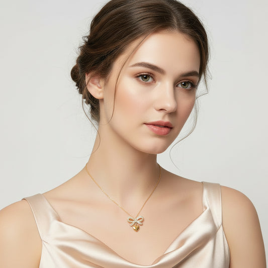A gold necklace with a bow-shaped pendant displayed on a white jewelry bust against a brown wood slat background.