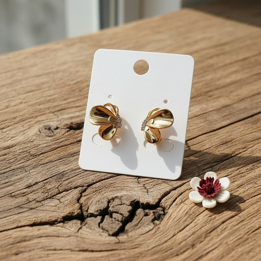 A pair of gold-toned bow-shaped stud earrings with small clear rhinestone accents, displayed on a white XUPING card over a white beaded tray and pink satin fabric.