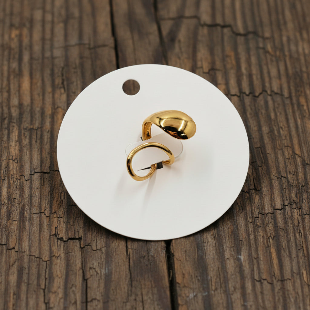 Gold earrings on a white card with 'Stainless Steel' text, against a pink fabric background