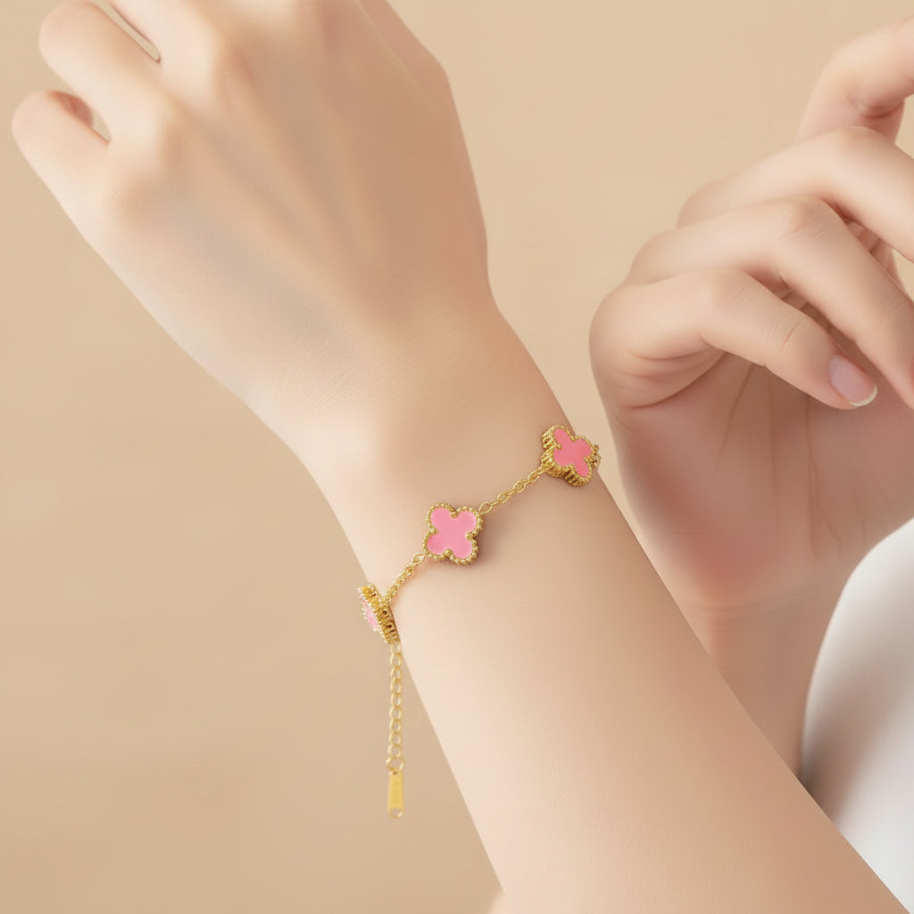 Gold bracelet with pink floral links on a light surface next to a perfume bottle.