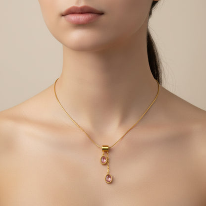 A gold chain necklace with two dangling oval pink gemstone pendants, displayed on a white beaded tray with pink fabric around it.